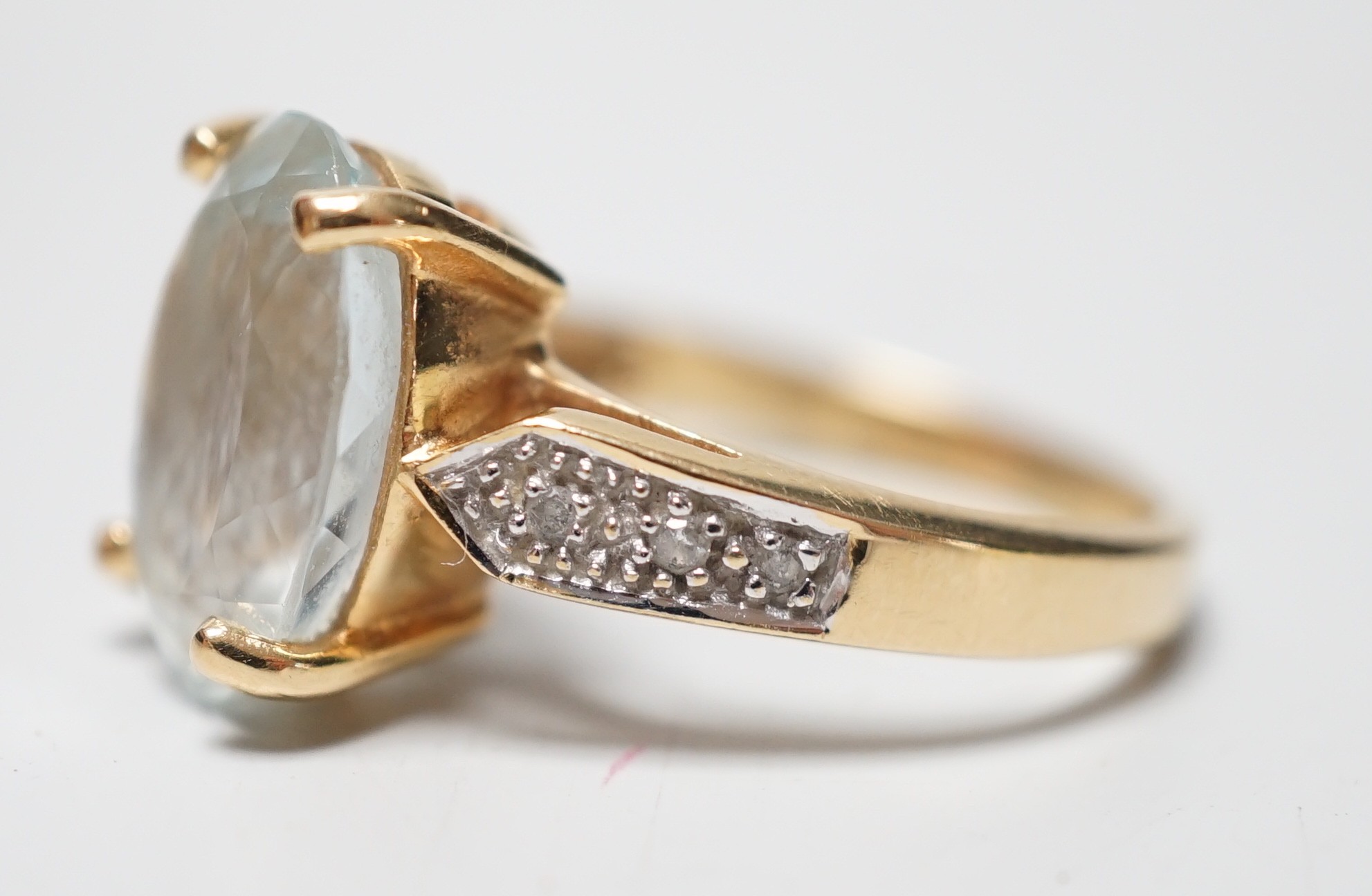 A modern 18ct gold and oval cut aquamarine set dress ring, with diamond chip set shoulders, size N, gross weight 5.5 grams.